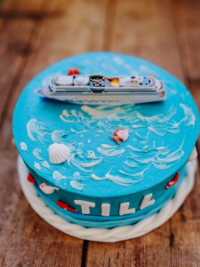 Runder Geburtstagstorte mit blauem Meer-Thema und einem Schiffsmodell obenauf.