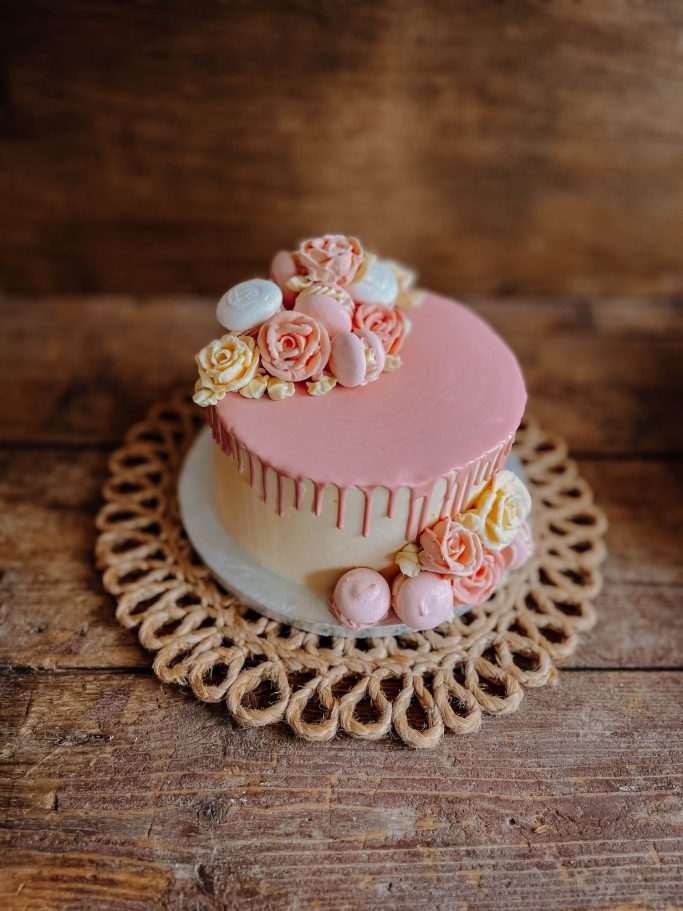 Runder Kuchen mit rosa Dekoration und Blumen auf einem dekorativen Untersetzer.