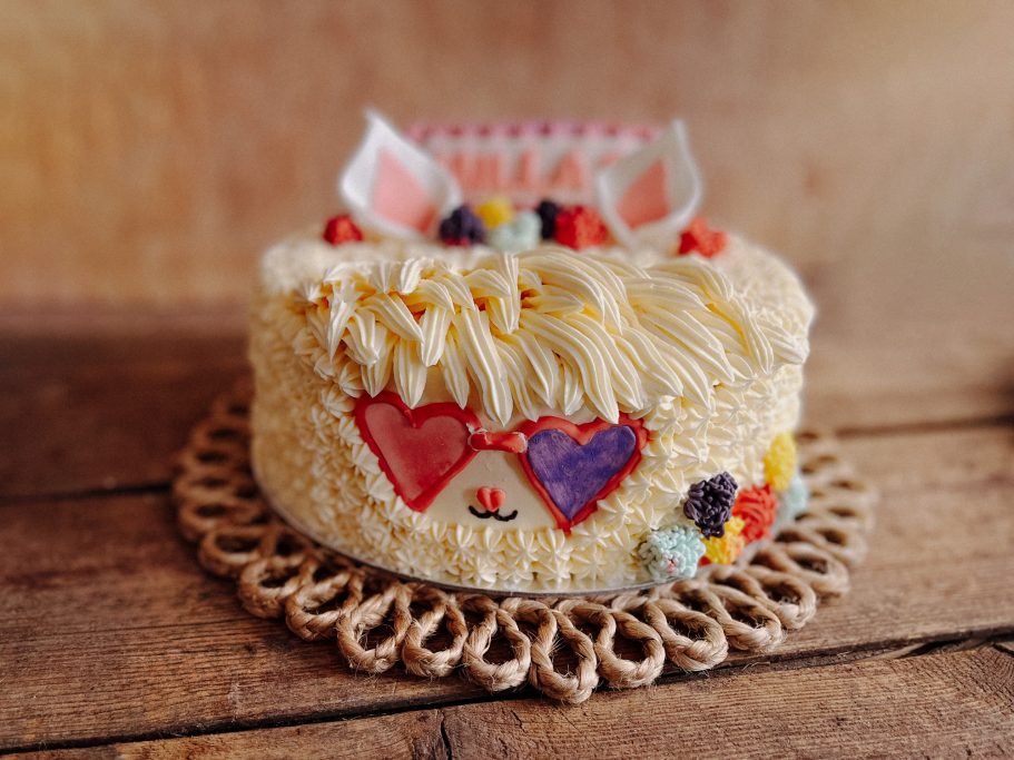 Helle, dekorierte Torte mit Herzmotiven und essbaren Blumen auf einem Holzuntergrund.