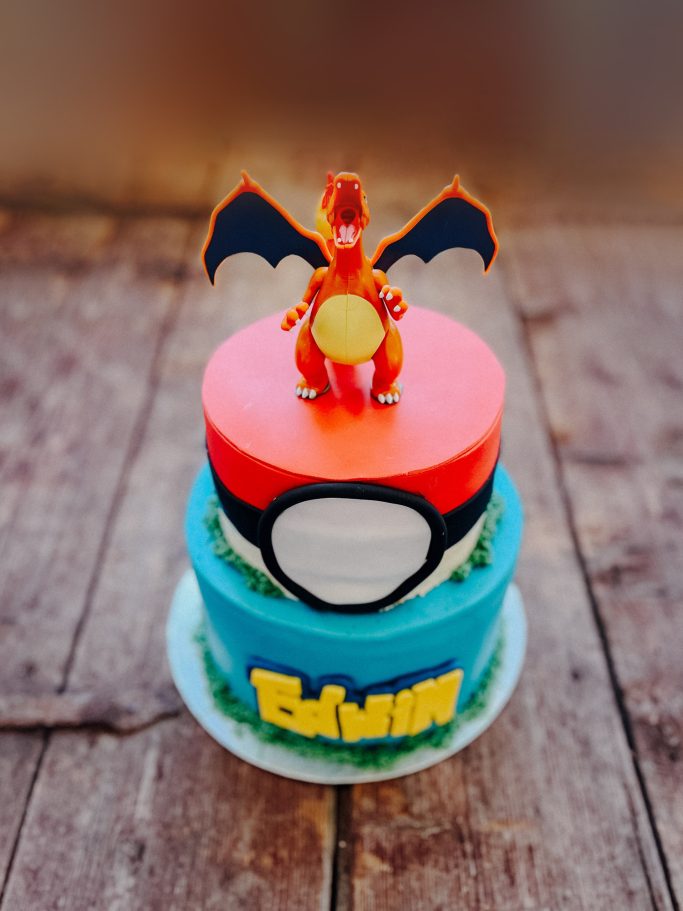 Zwei-stöckiger Geburtstagskuchen mit Pokémon-Thema und einem Charizard-Dekor.