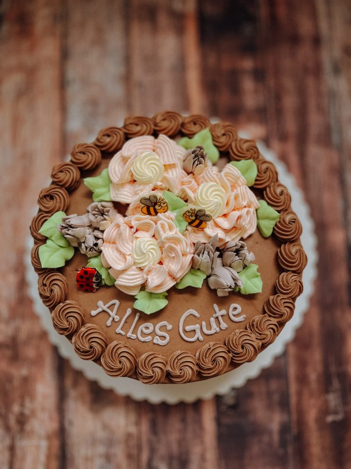 Schokoladentorte mit bunten Blüten und „Alles Gute“ in der Mitte.