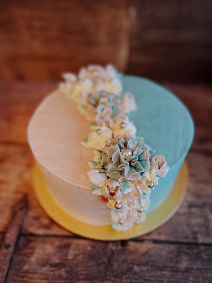 Zweifarbiges Törtchen mit floralen Dekorationen auf einer rustikalen Holzoberfläche.