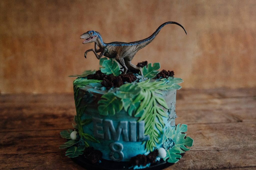 Eine Geburtstagstorte mit Dinosaurier-Figur und grüner Dekoration.