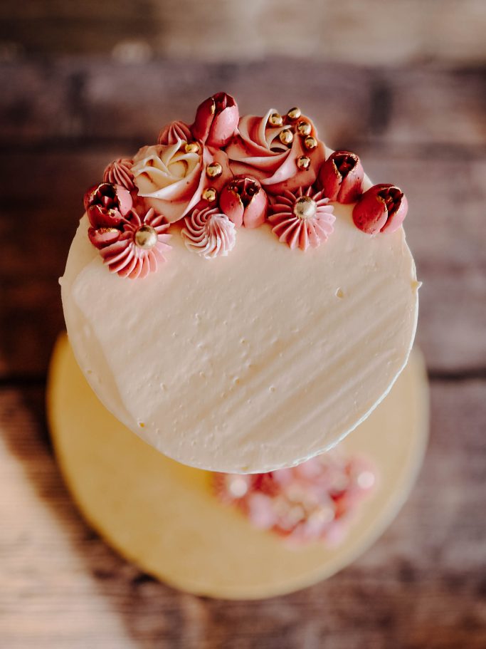 Torte mit rosa und weißen Verzierungen auf einem rustikalen Holzuntergrund.