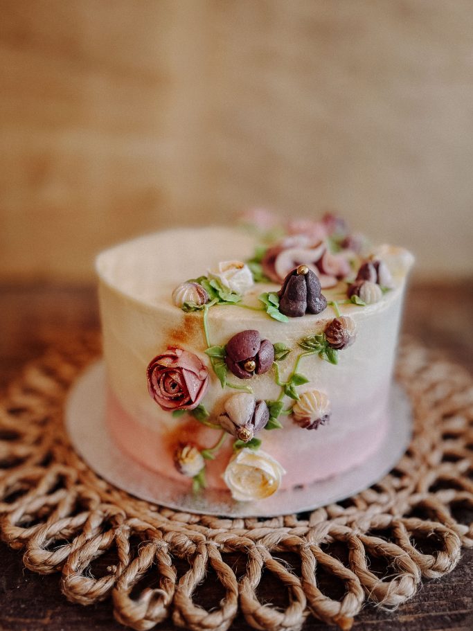 Torte mit zartem Rosé- und Weißton, dekoriert mit frischen Blumen und filigranen Details.