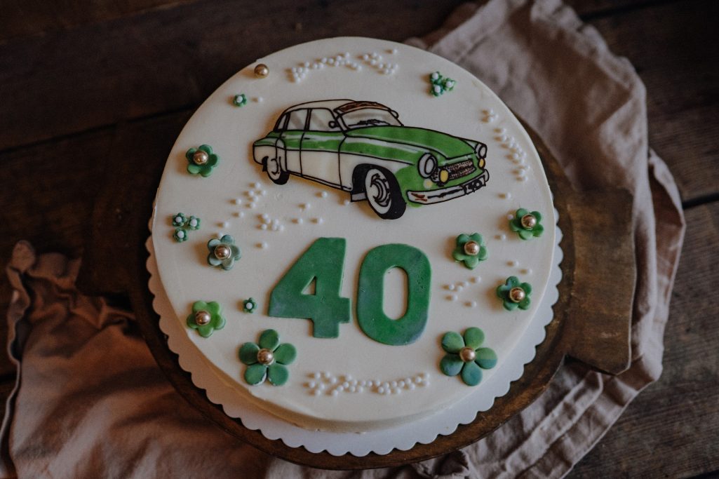 Torte mit grünem Auto-Design und der Zahl 40, verziert mit kleinen Blumen.