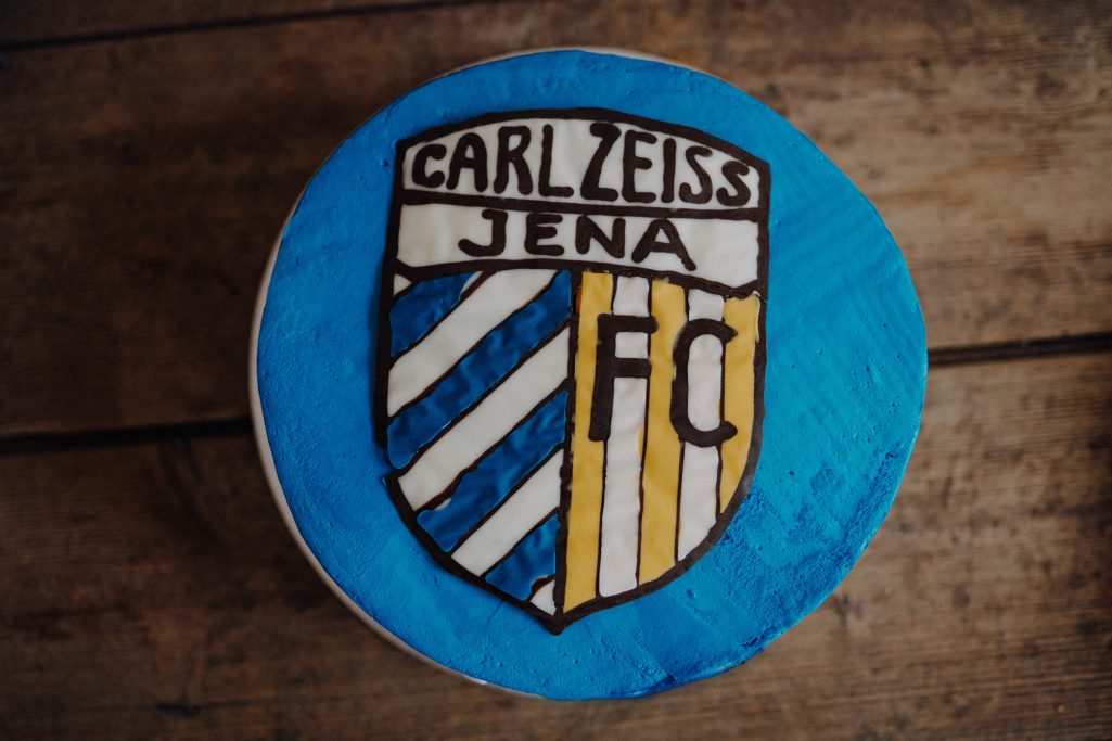 Wappen des FC Carl Zeiss Jena auf blauer Hintergrundfarbe mit Streifen.