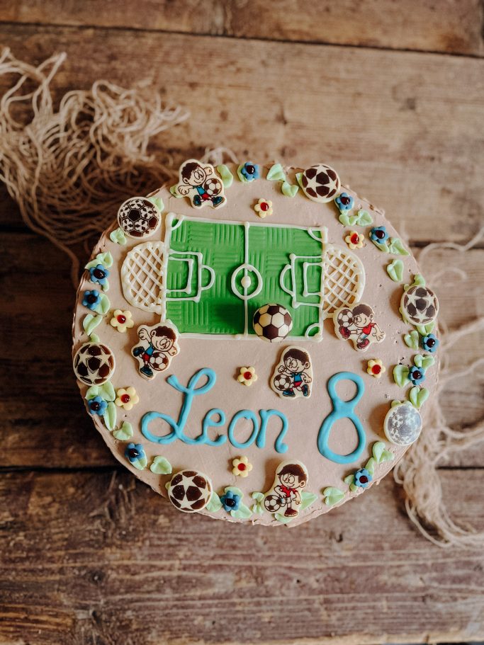 Runder Geburtstagskuchen mit Fußballfeld, Namen "Leon" und bunten Verzierungen.