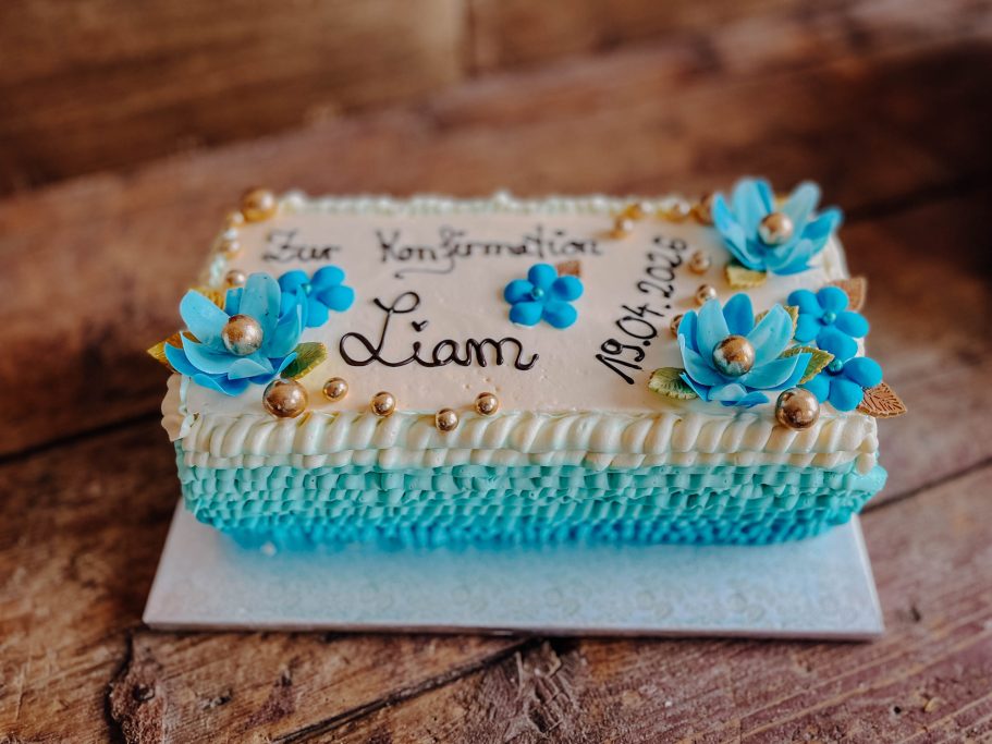Eine Torte mit blauen Blumen und goldenen Akzenten, beschriftet mit "Liam".