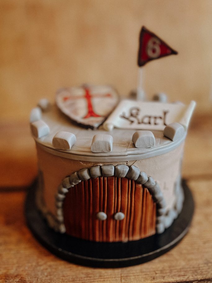 Geburtstagskuchen in Form einer Burg mit Flagge und Wappen, herzlich dekoriert.