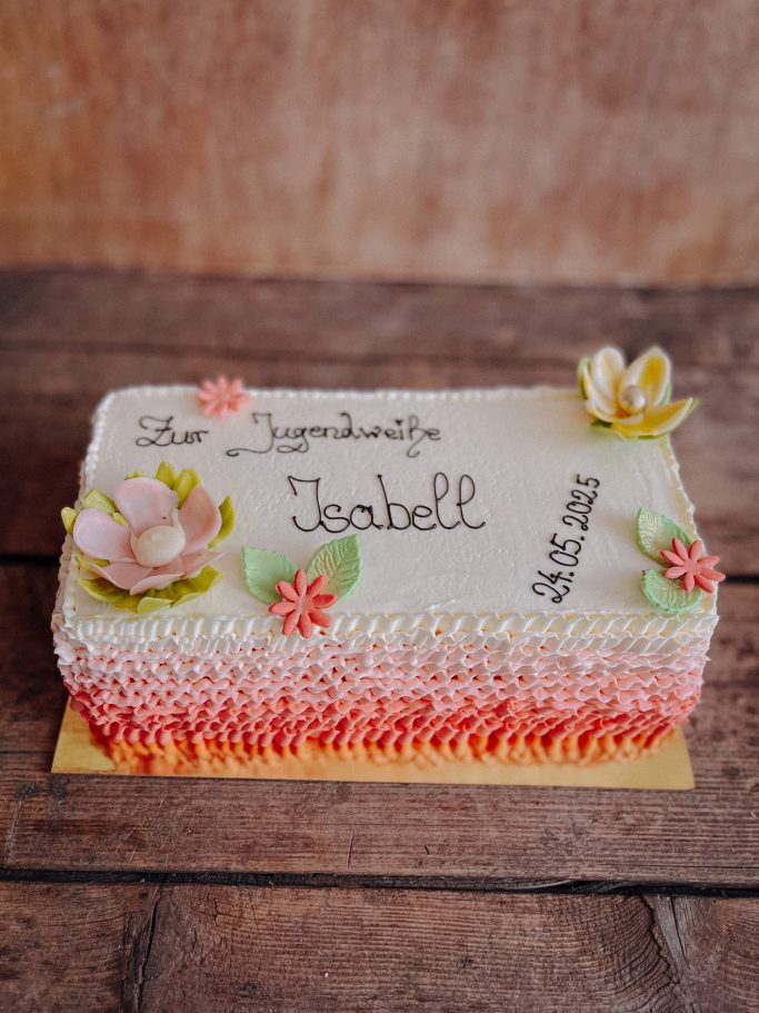 Torte mit weißen und rosa Dekorationen, Blumen und dem Namen "Isabell" darauf.