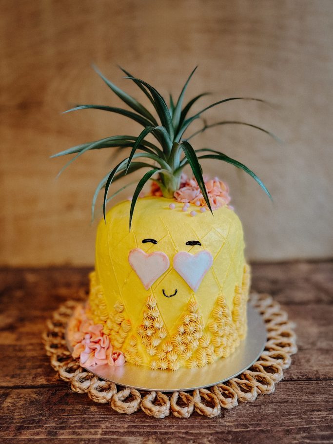 Fröhlicher Kuchen in Ananasform, dekoriert mit einer Pflanze und essbaren Herzchen.
