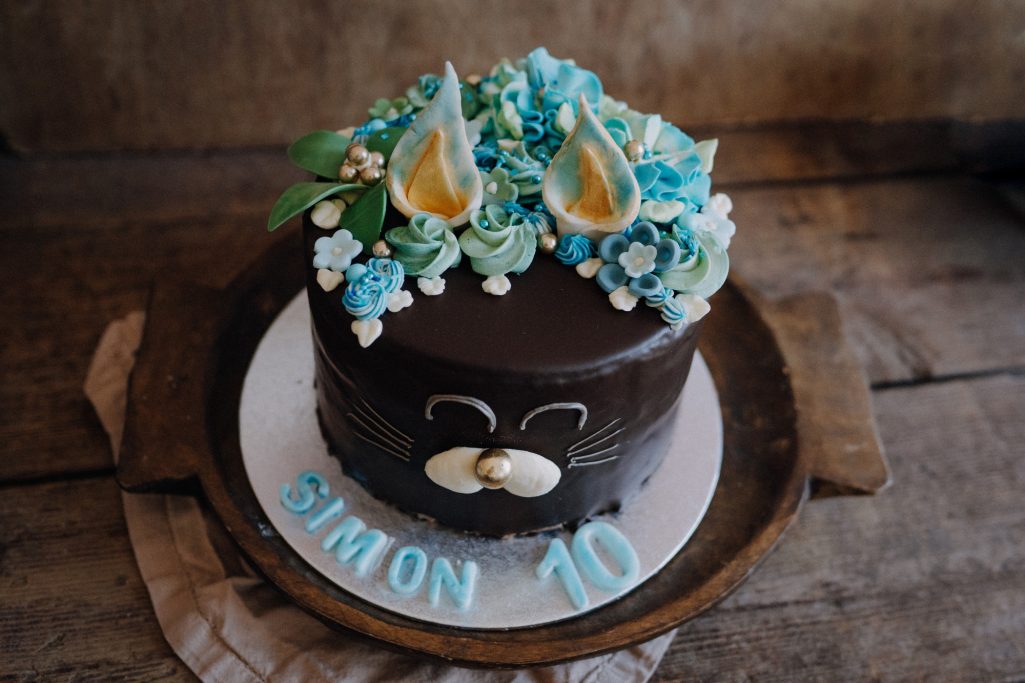 Schokoladentorte mit bunten Blumen und der Aufschrift "Simon 10" auf dem Rand.