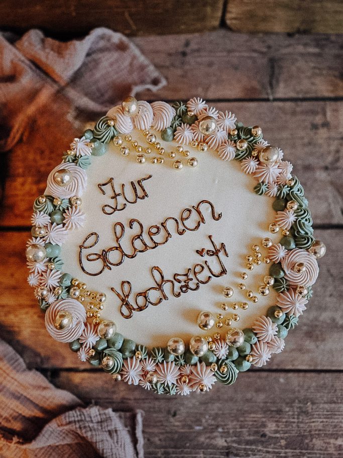Torte mit Schriftzug „Zur Goldenen Hochzeit“ und dekorativen Verzierungen.