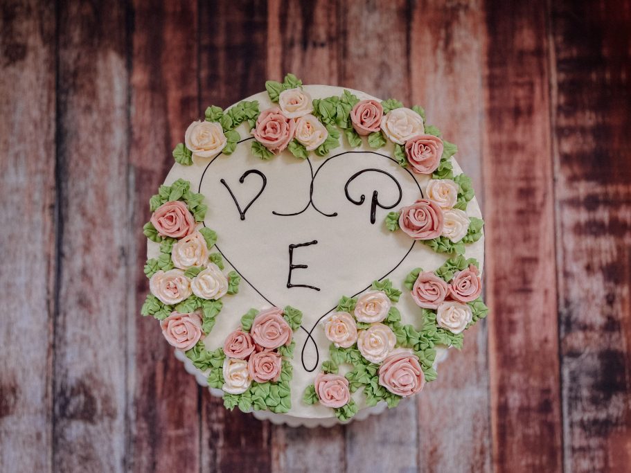 Kreisförmiger Kuchen mit Herzmuster und Rosendekoration in Rosa und Grün.