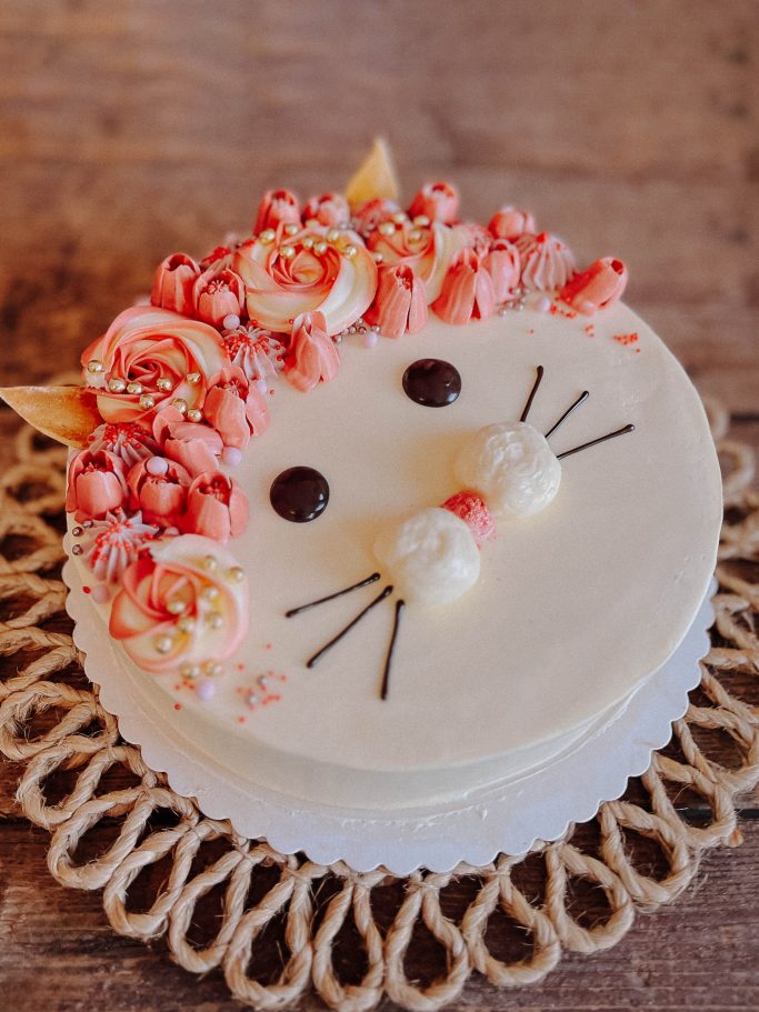 Kuchen mit Katzenmotiv, dekoriert mit rosa Blumen und Schokoladenaugen.