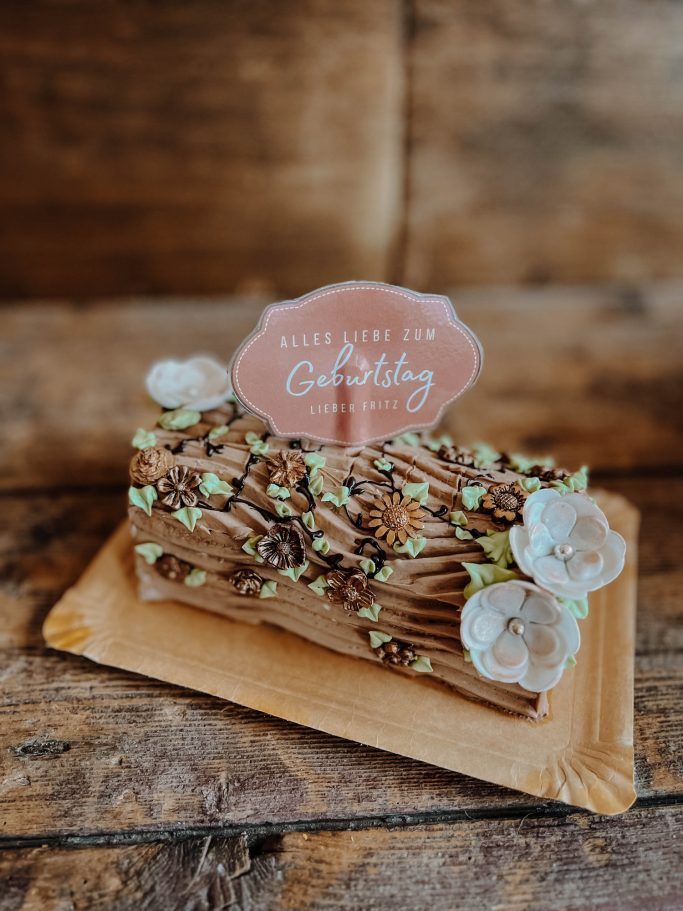 Eine Schokoladen-Buche mit Zuckerdekoration und einer Geburtstagskarte obenauf.