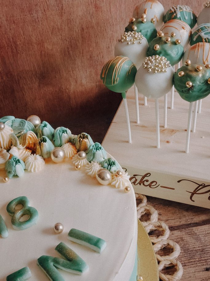 Torte mit grünem Dekor und Cake Pops, verziert mit Gold- und Perlendetails.