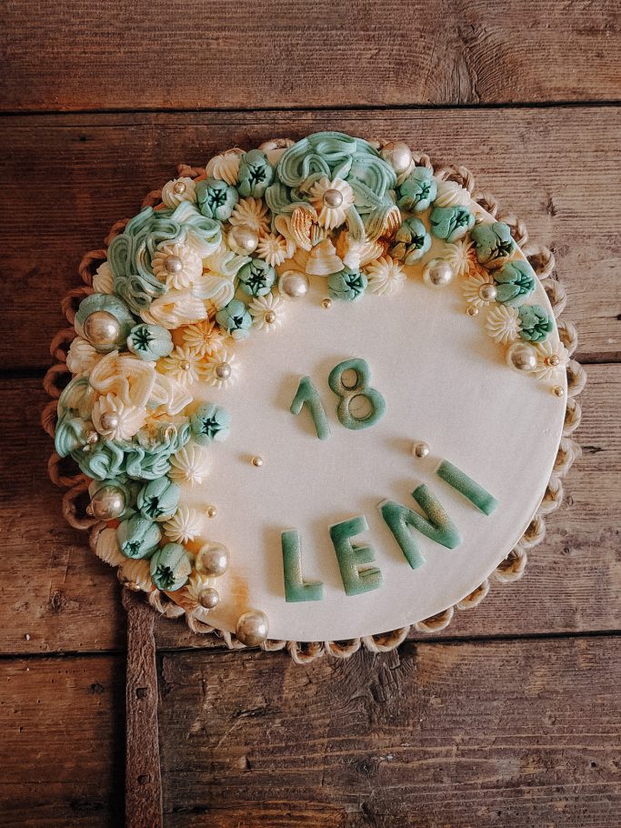 Geburtstagstorte mit der Aufschrift „18 Leni“ und dekorativen Cremeblumen.
