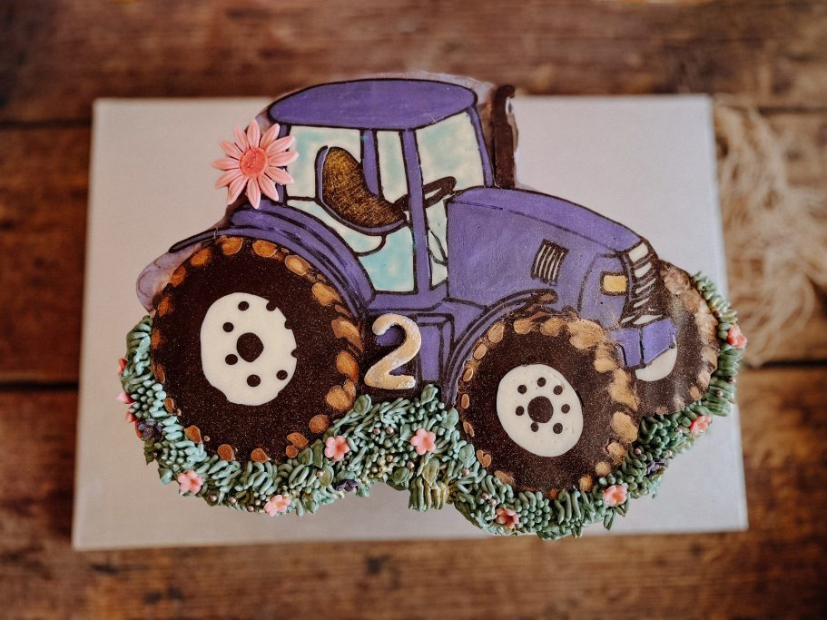 Lila Traktortorte mit Blumenverzierungen und der Zahl „2“ auf einem Holztisch.