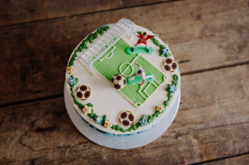 Süßer Fußballkuchen mit Rasen, Tor und Spielerfiguren dekoriert.