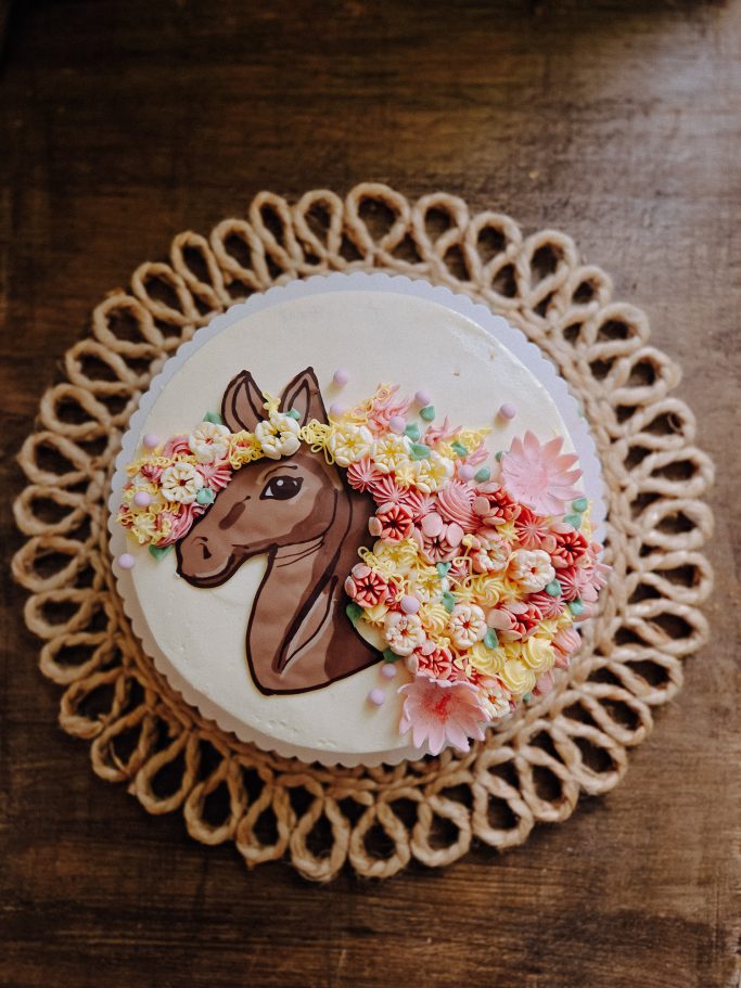 Torte mit Pferdekopf aus Zuckerguss und bunten Blüten dekoriert.