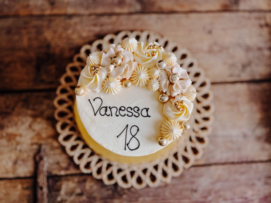 Torte mit der Aufschrift "Vanessa 18" und dekorativen Blüten auf einem Holzuntergrund.