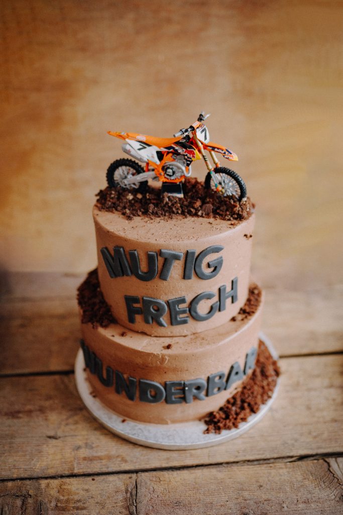Torte mit zwei Schichten, orangefarbener Motorradfigur und Aufschrift: "Mutig, Frech, Abenteuer".