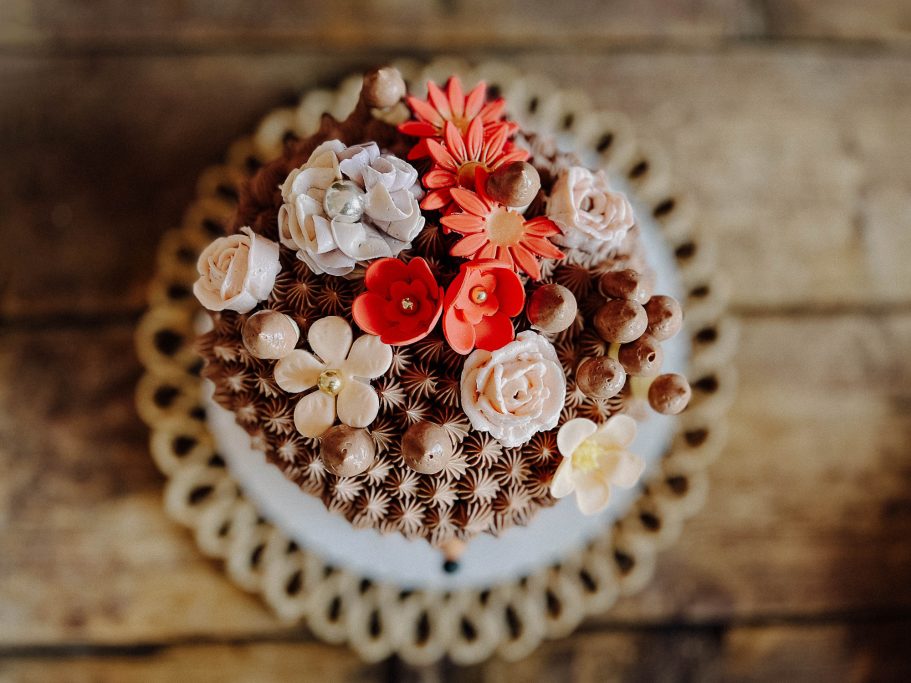 Schokoladenkuchen mit bunten Blüten und dekorativen Perlen auf einem Holzuntergrund.